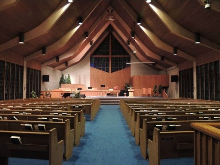 Interior of a contemporary Mennonite church sanctuary with wooden pews, hymnals, a simple stage, and natural lighting.