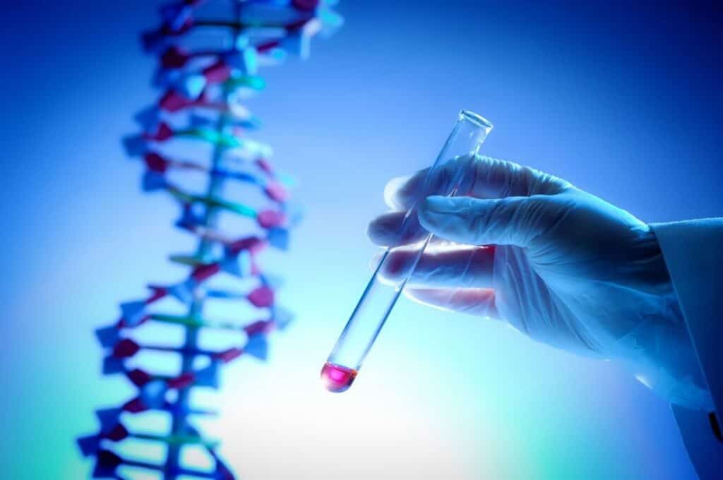 Close-up of a gloved hand holding a test tube against a DNA double helix illustration.