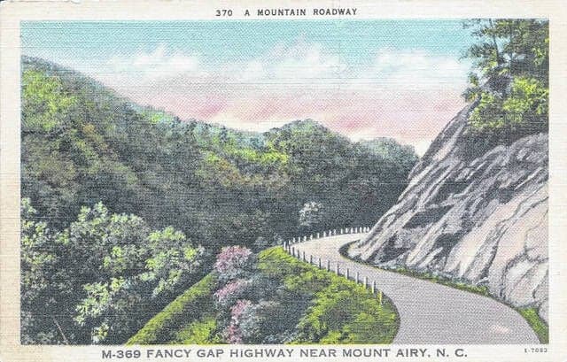 Vintage postcard of the Fancy Gap Mountain highway near Mount Airy showing a curved road along wooded slopes.
