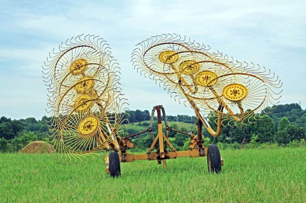 A yellow wheel rake stands in a hayfield, used to pull dried hay into rows before baling.
