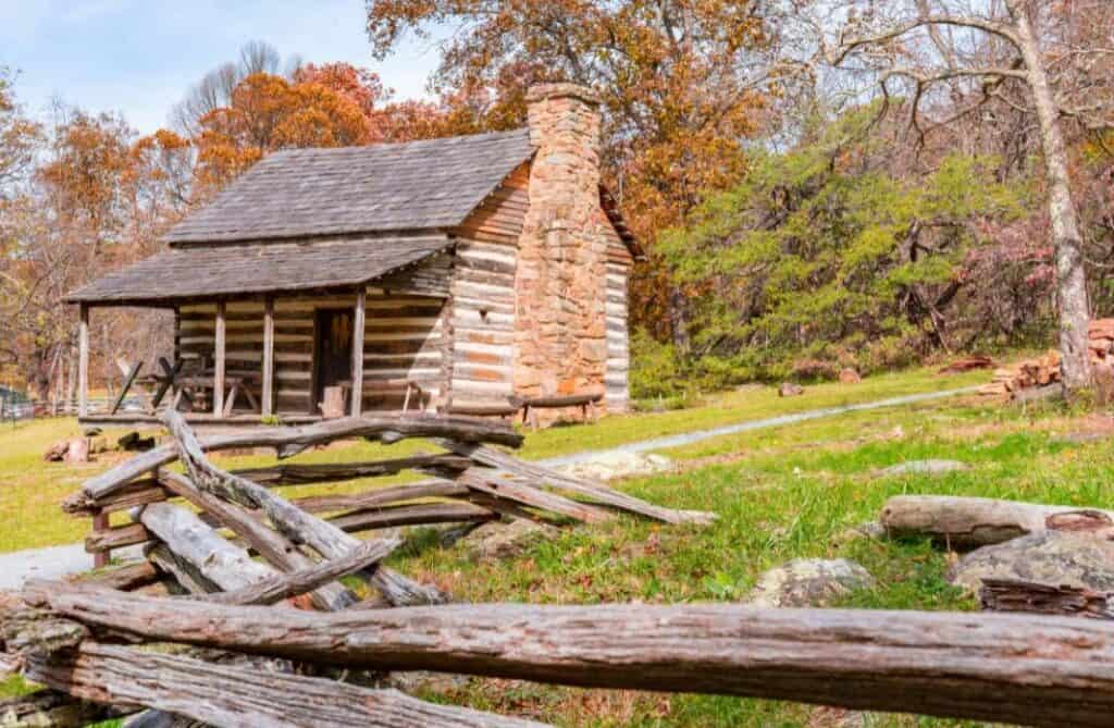 Historic Appalachian cabin surrounded by split-rail fencing and autumn hills.