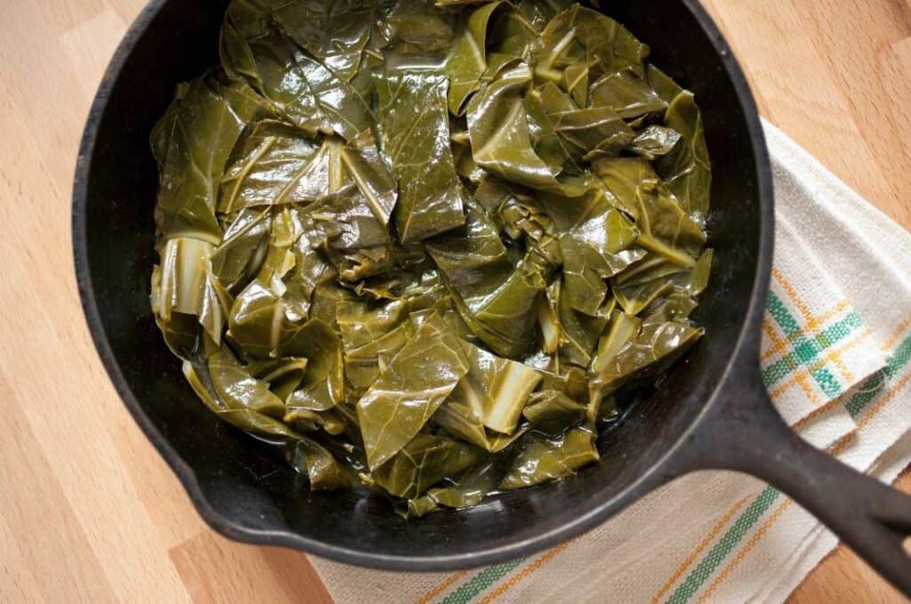 Collard greens simmered in a cast-iron skillet, softened after long cooking.