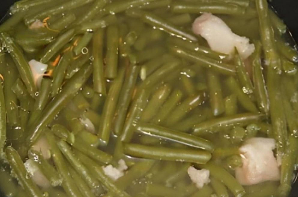 Green beans simmering in a pot with softened chunks of fatback for seasoning.