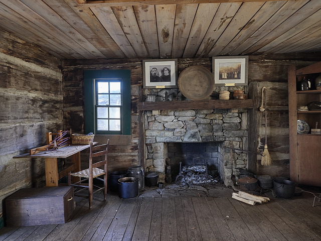 Historic Appalachian cabin interior showing a small window beside a stone fireplace.