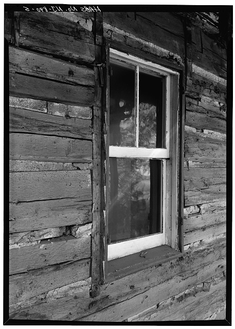 Close-up of a historic log cabin window set into weathered wooden walls.