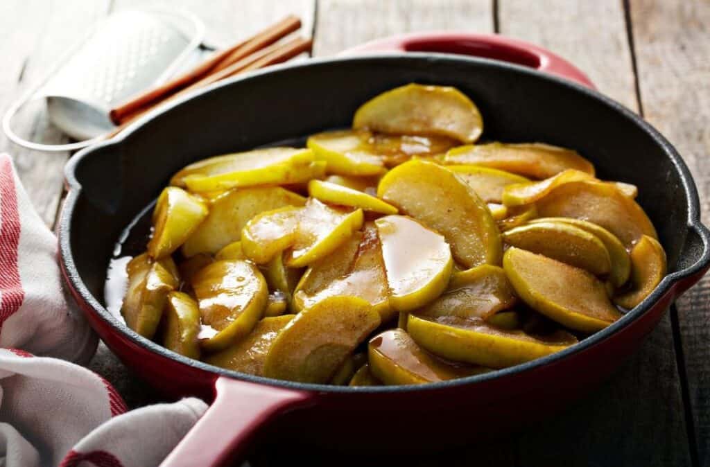 Sliced apples cooking in a cast iron skillet with brown sugar and butter.