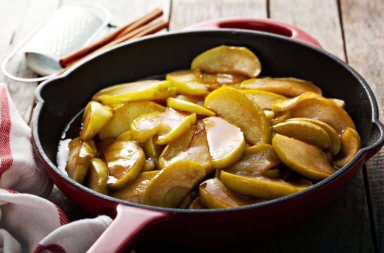 Sliced apples cooking in a cast iron skillet with brown sugar and butter.