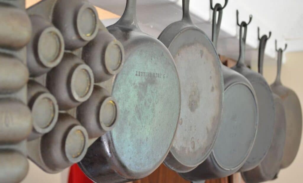 Well-used cast iron skillets hanging from hooks in a kitchen.