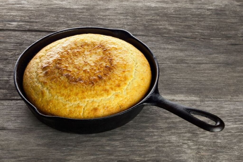 Cornbread baked in a cast iron skillet with a crisp crust that shows classic cast-iron flavor.