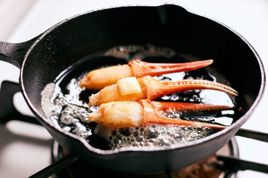 Cast iron skillet with crab legs sautéing in butter on a stovetop.