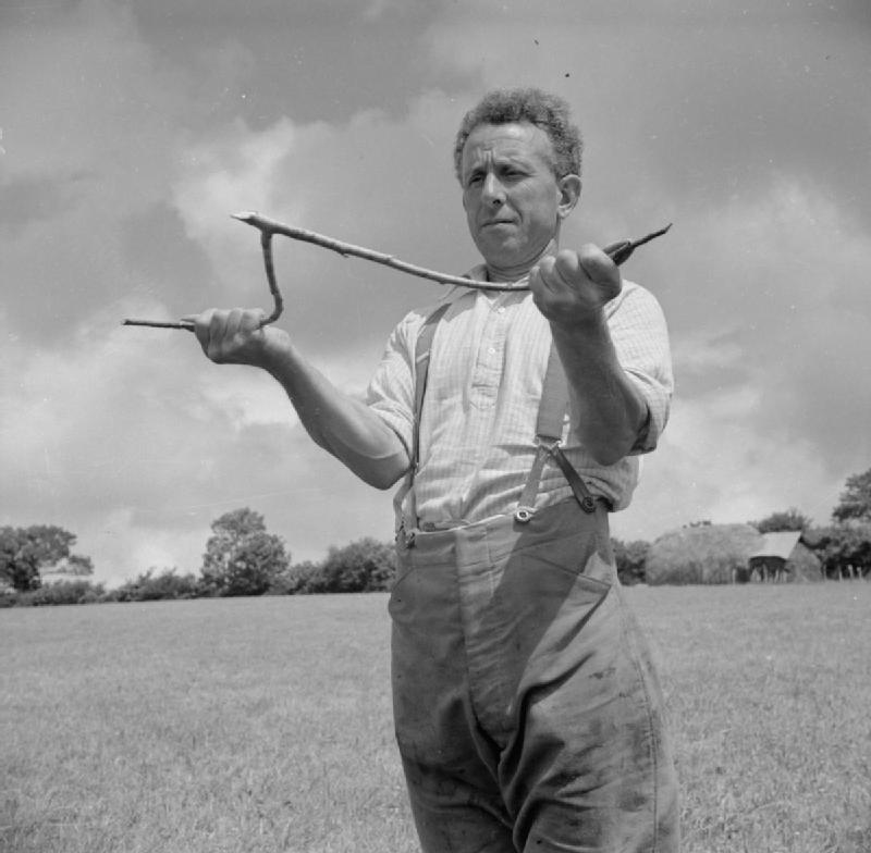 A man holding a forked branch in a historic dowsing demonstration.
