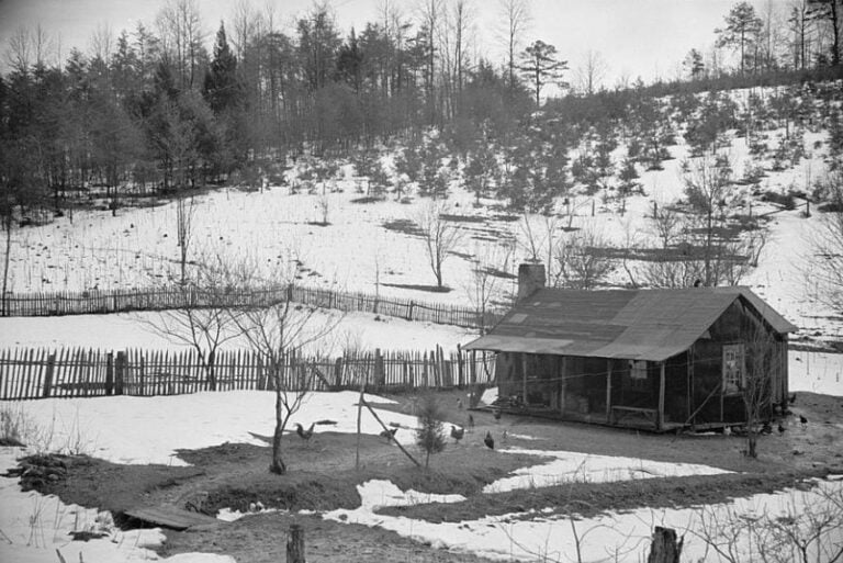 Appalachian farmhouse in winter showing a fenced yard, outbuildings, and snow-covered hillside.
