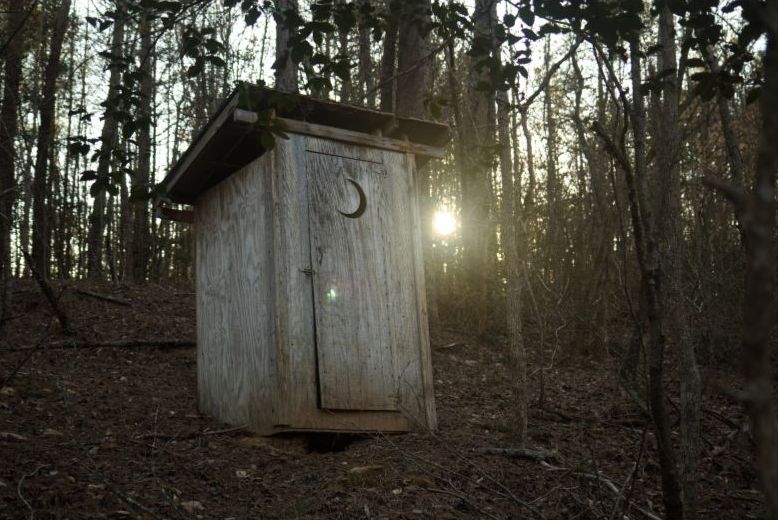 Wooden outhouse in wooded yard at sunrise