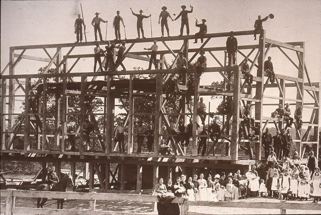 Appalachian work gathering during a community barn raising with dozens of neighbors raising the timber frame together
