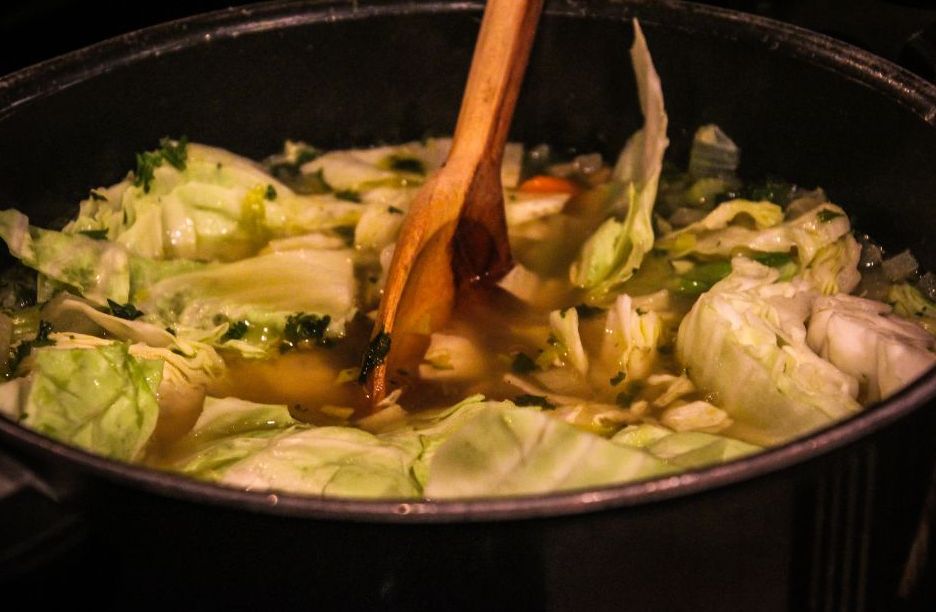 Cabbage simmering in a pot with broth and herbs