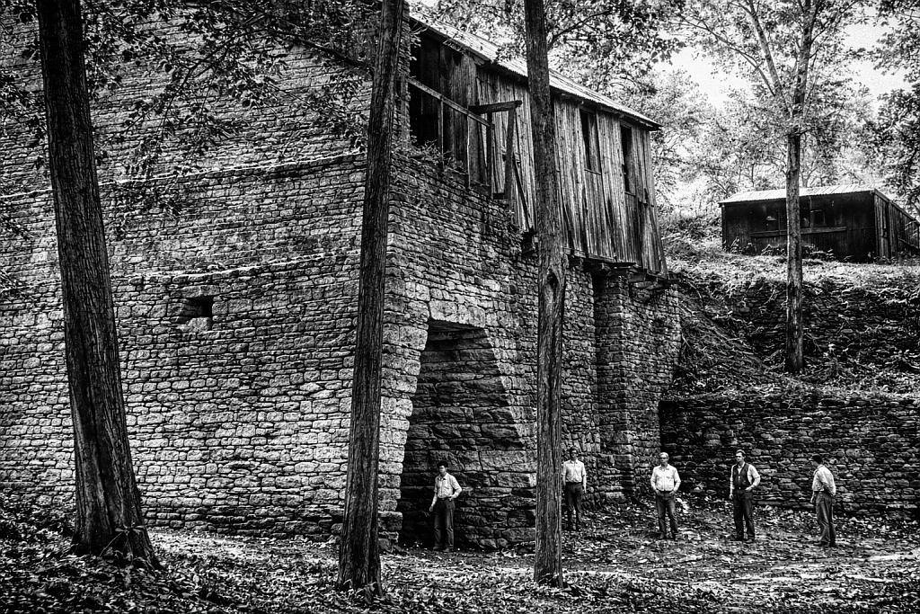 Historic iron furnace workers standing near stone stack and work area