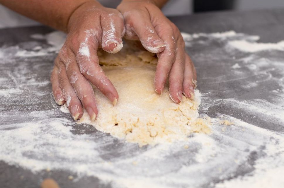 Hands mixing biscuit dough on a floured surface in a mountain pantry kitchen