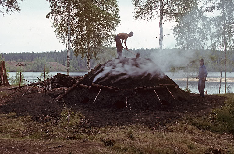Workers tending a historic charcoal burn used controlled airflow to convert wood into charcoal for iron production.