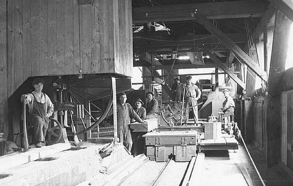 Sawmill workers standing beside machinery inside a lumber mill