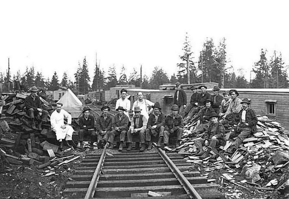 Timber company workers gathered beside railroad tracks at a logging camp