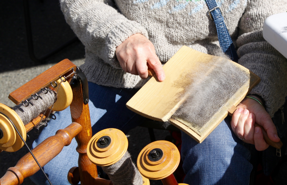 Person using hand cards to prepare wool beside spinning equipment